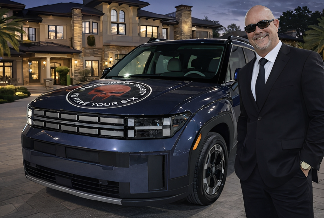 A man in sunglasses stands next to a dark blue electric car in front of a luxury house at dusk.